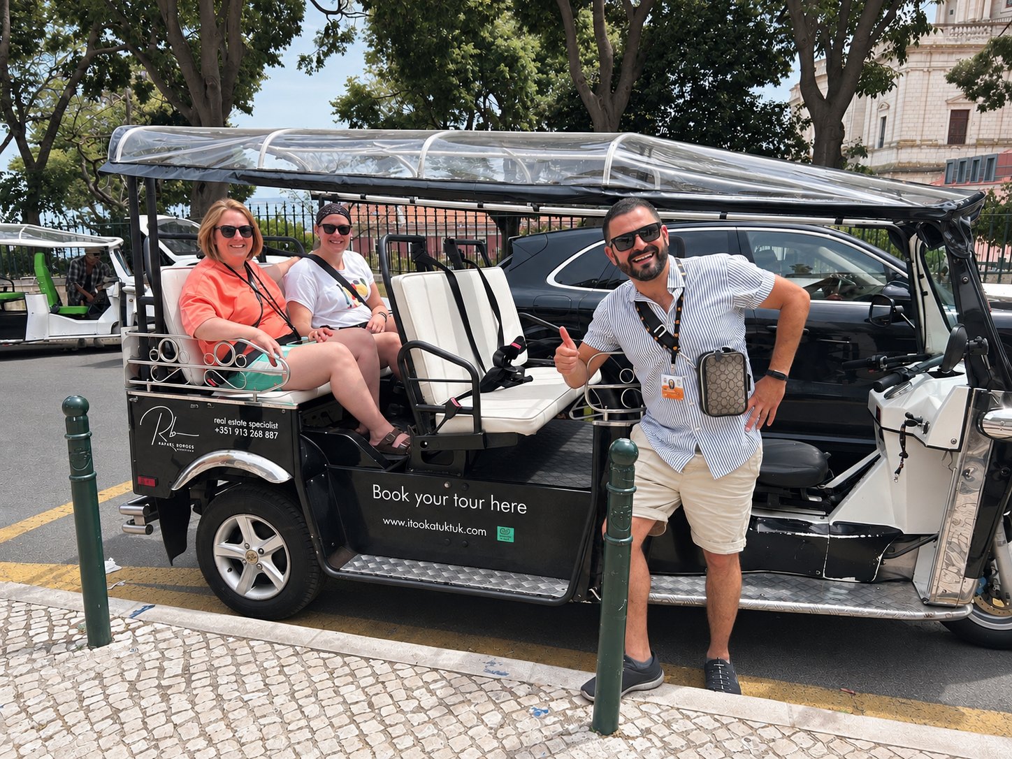 A smiling guide giving a thumbs-up beside two guests seated in a tuk tuk