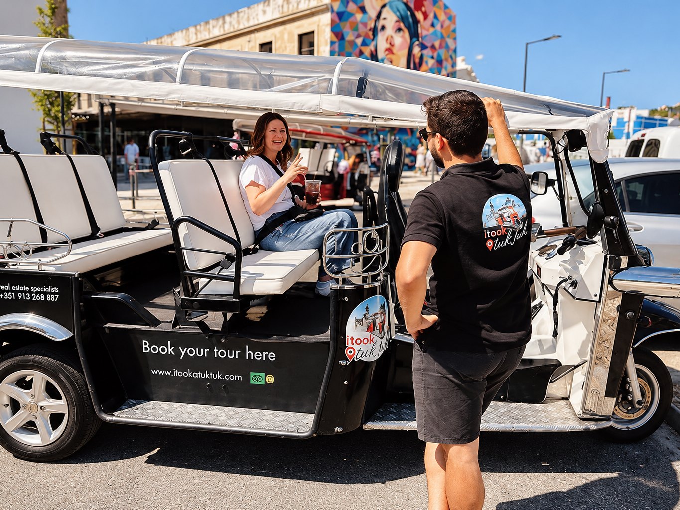 A guide chatting with a guest seated in a tuk tuk beside a colourful Lisbon mural