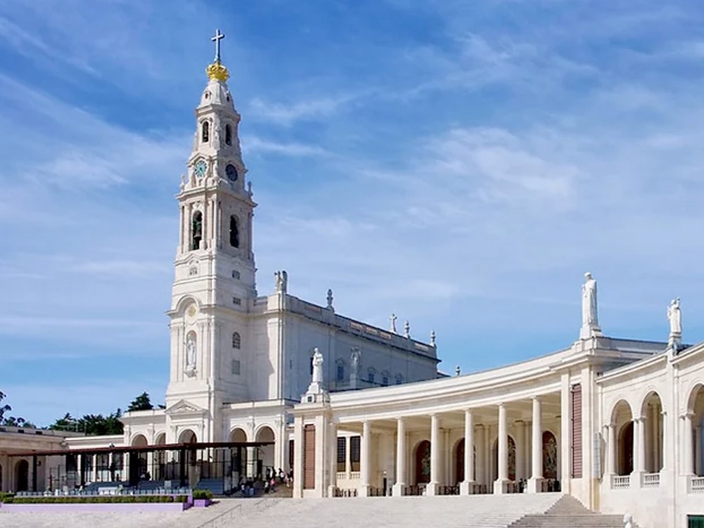 The basilica tower and colonnade of the Sanctuary of Fátima under a blue sky