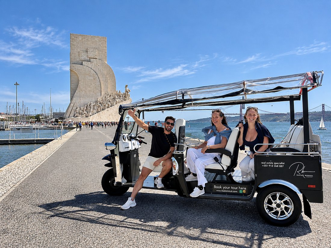 An electric tuk tuk with guests beside the Padão dos Descobrimentos in Belém