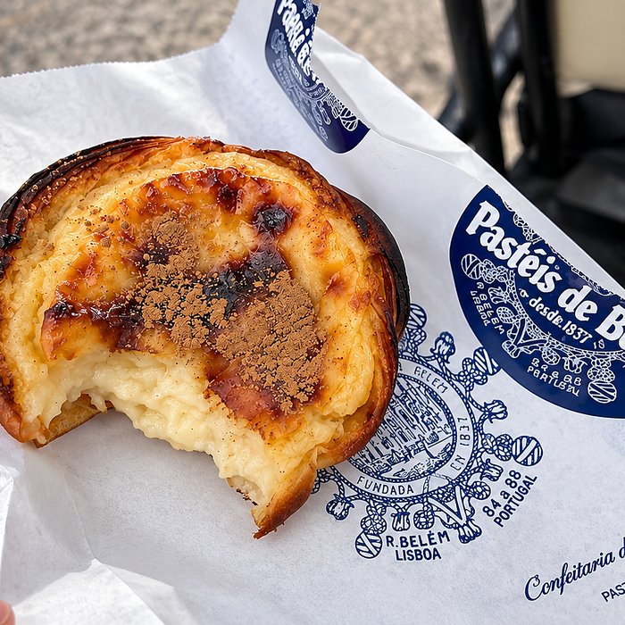 A Pastél de Belém with a bite taken out of it, in its branded Pastéis de Belém wrapper