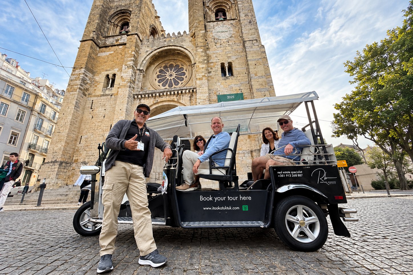 A guide giving a thumbs up beside a private electric tuk tuk full of guests in front of Lisbon Cathedral