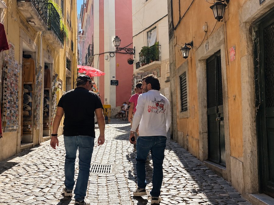A narrow cobbled Lisbon street with people walking between pastel buildings