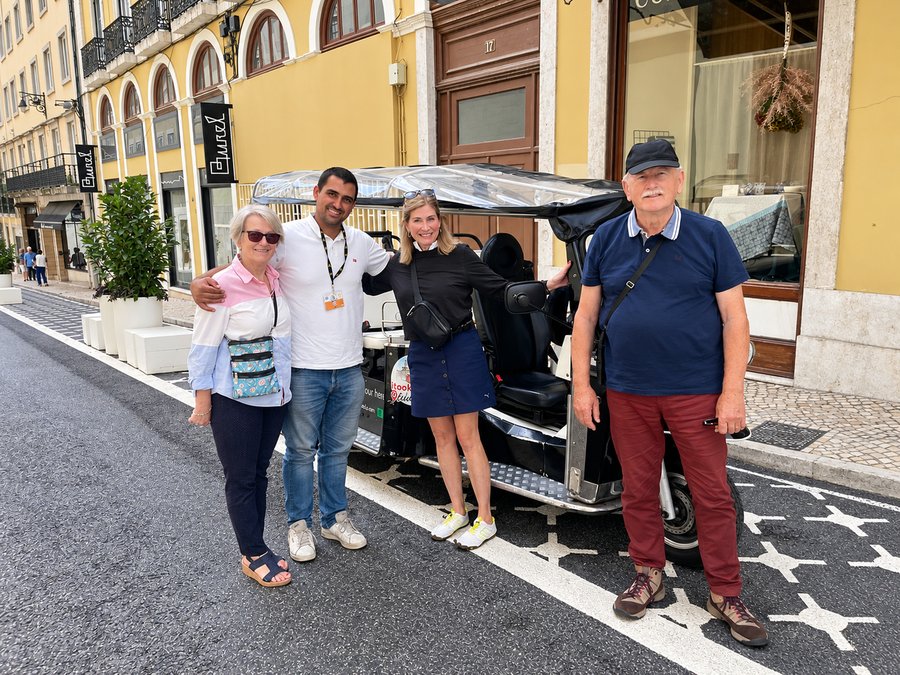 A guide with guests beside a tuk tuk on a Lisbon street