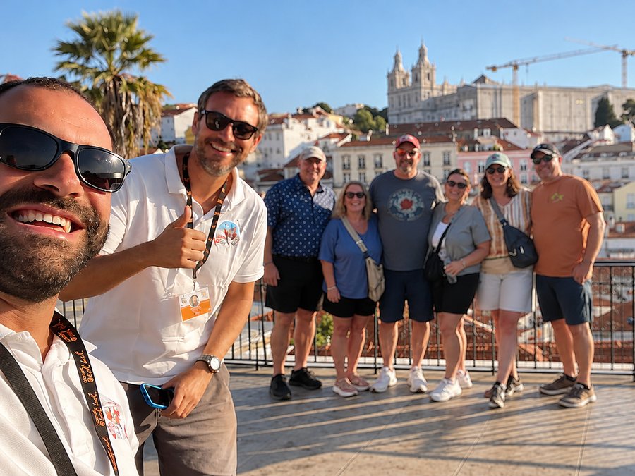A guide taking a selfie with eight guests at a Lisbon miradouro, the Alfama rooftops behind them